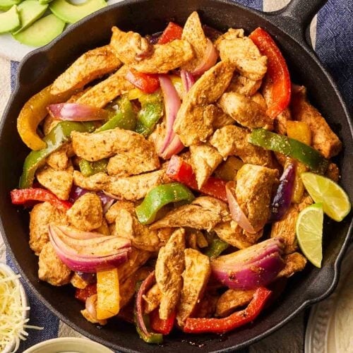 A pan of chicken fajitas with peppers and lime, on a table ready to be served.