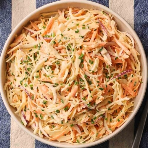 A bowl of coleslaw on a table with a blue and white stripy tablecloth.