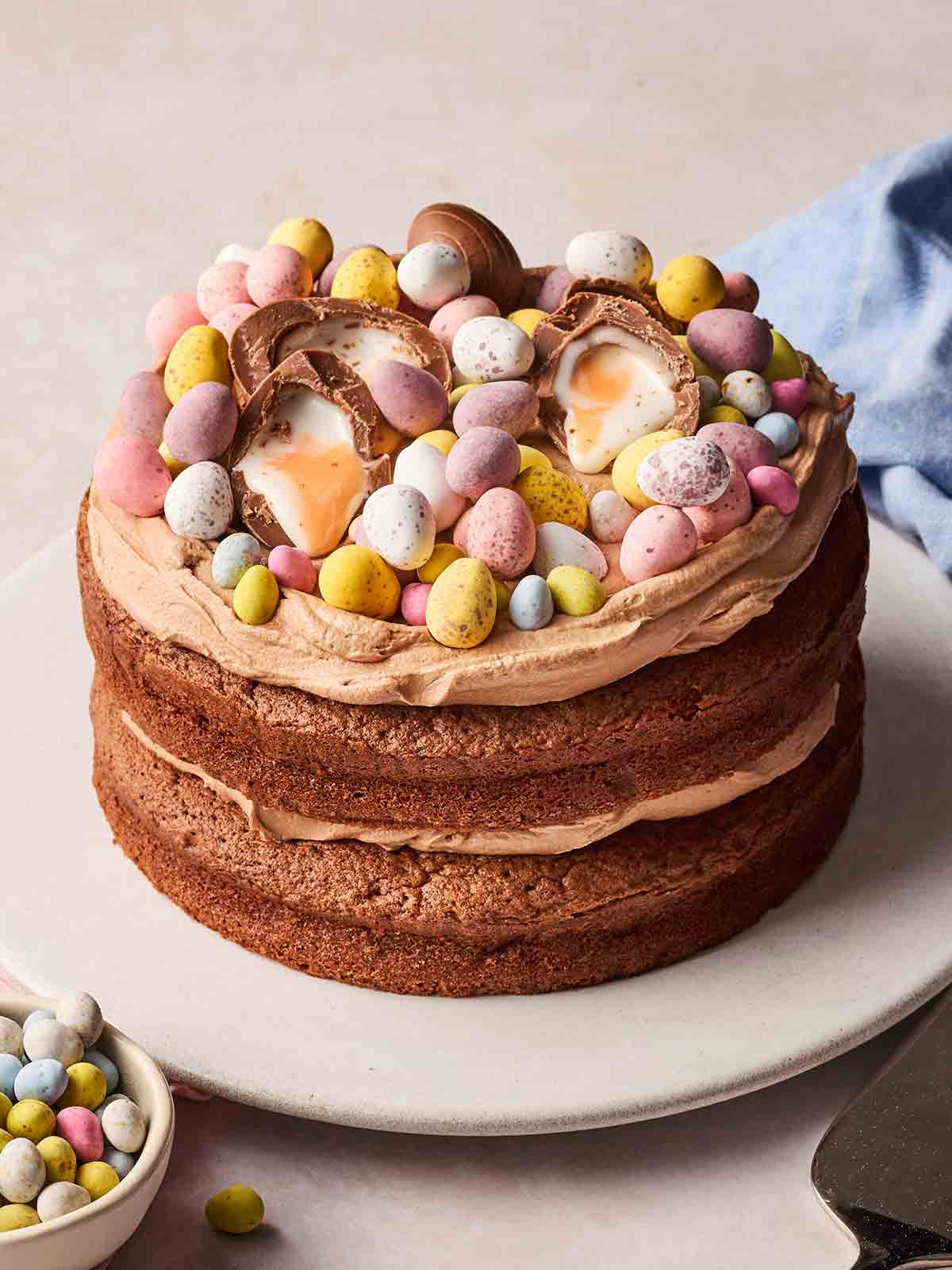 An easter chocolate cake on a plate, with lots of mini eggs on top for decoration.