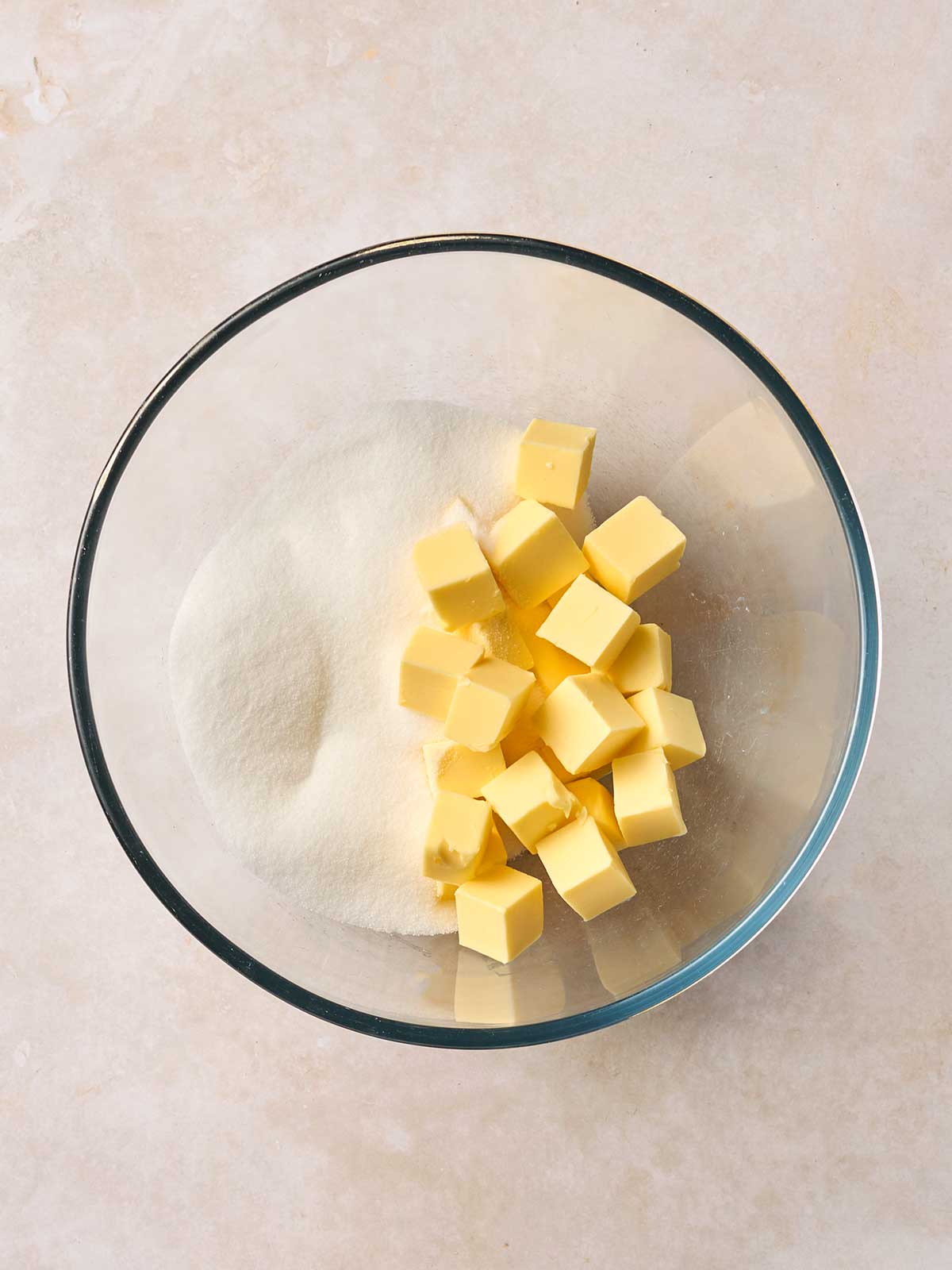 A glass bowl with cubes of butter and sugar on a white surface.