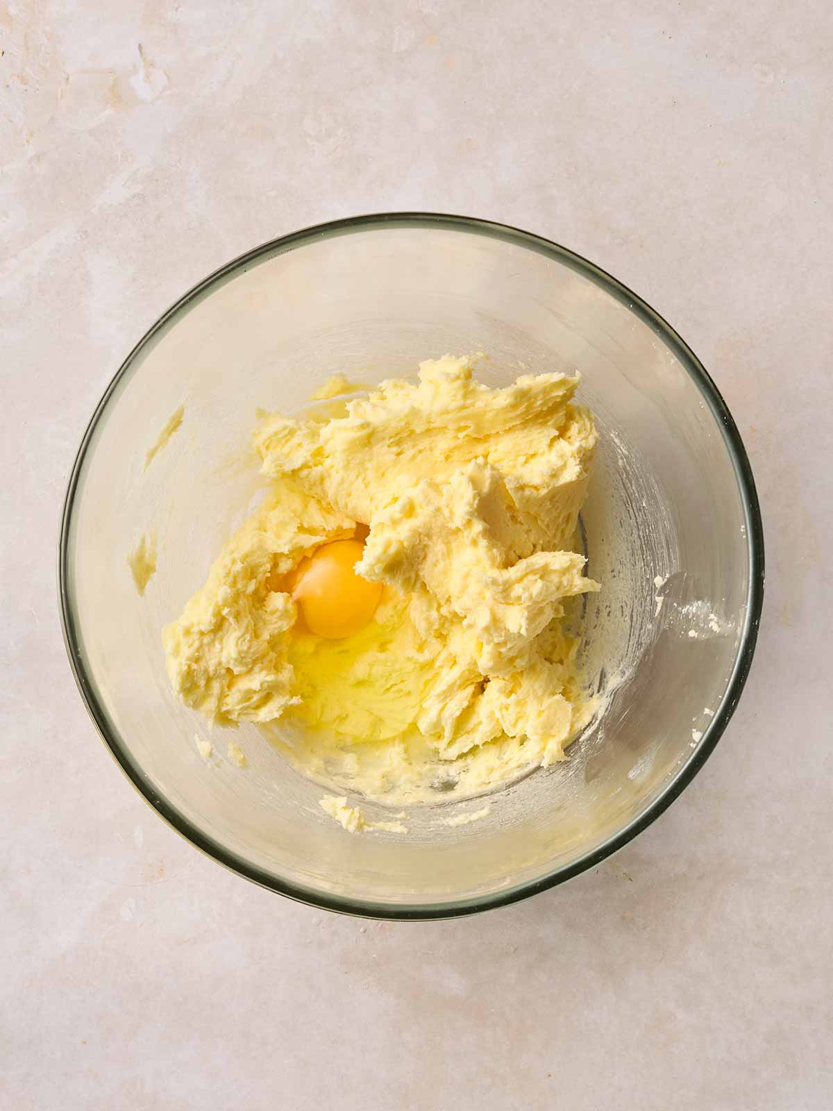 Creamed sugar and butter in a glass bowl on a white surface, with an egg inside.