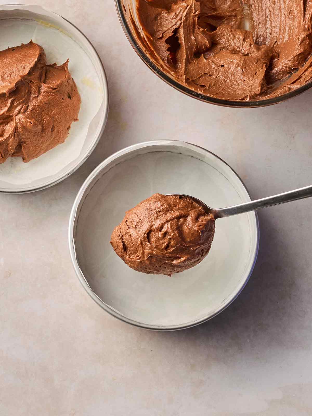 A spoon putting chocolate cake into two tins, ready to bake.