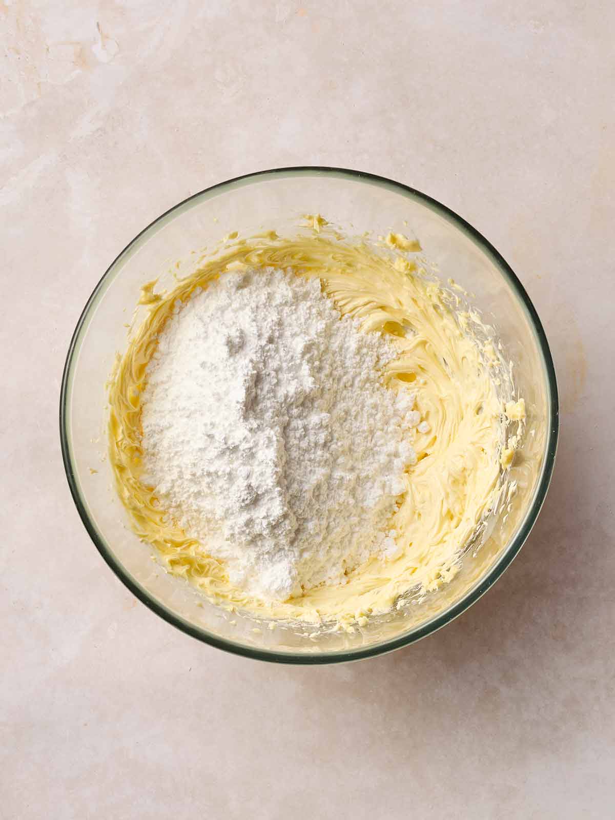 Buttercream in a glass bowl with icing sugar on top, ready to be mixed in.