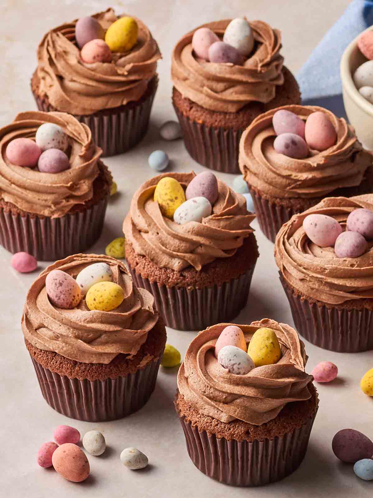 A batch of Chocolate Easter Cupcakes with mini eggs on top on a white surface.