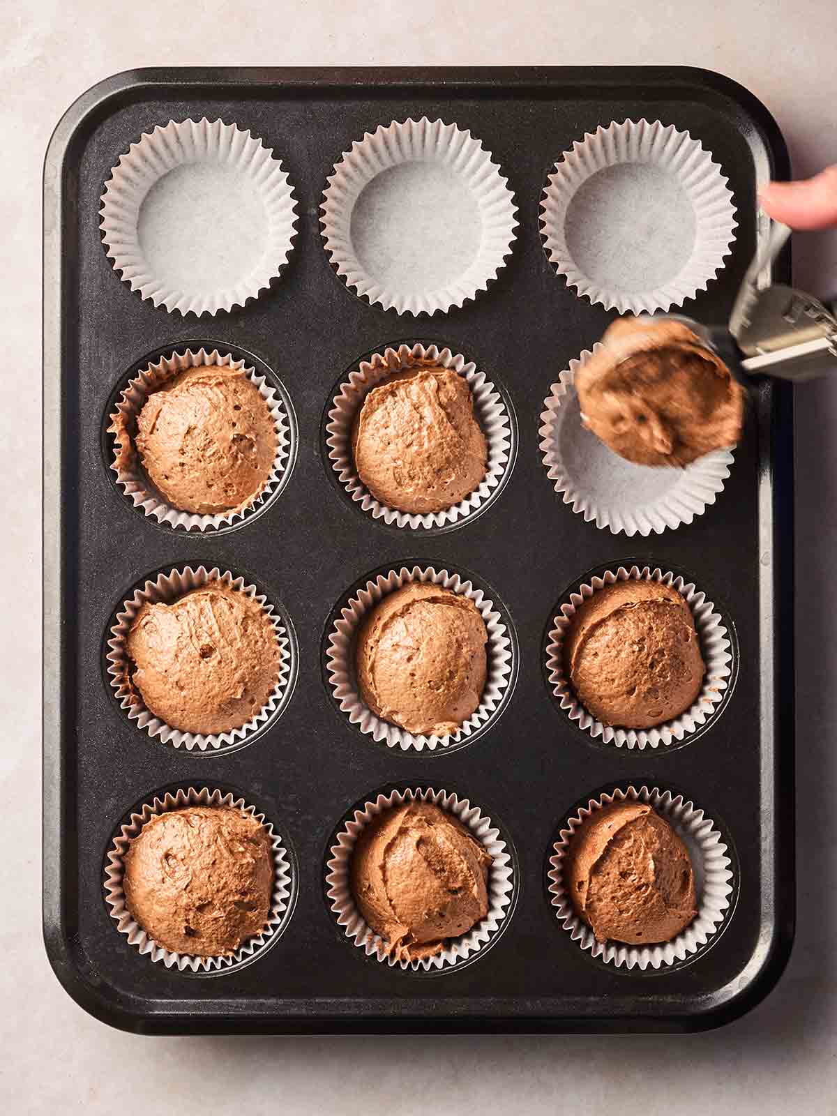 A muffin tray on a white surface, with half of them filled with chocolate Easter cupcake batter.