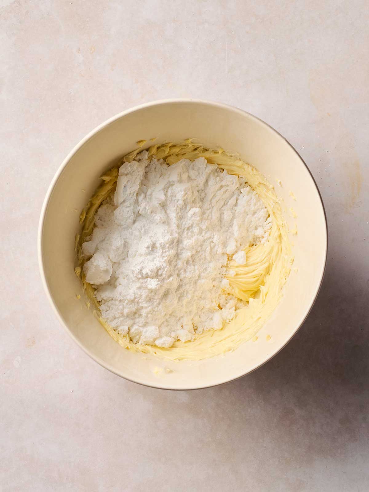 Cream butter with icing sugar on top in a bowl, on a white surface.