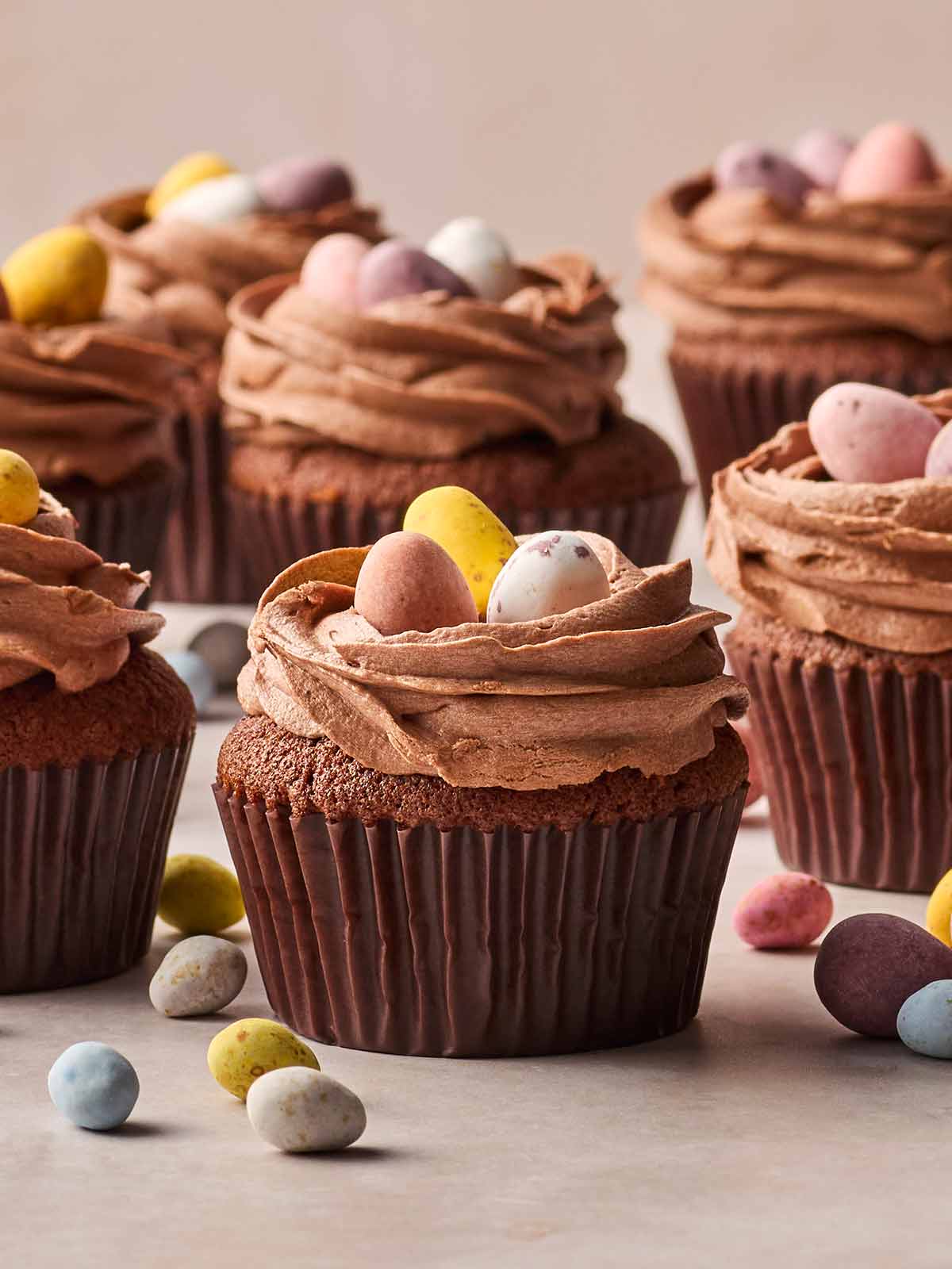 A batch of Chocolate Cupcakes from these side, with Cadbury's Mini Eggs on top and some scattered on the surface beneath.