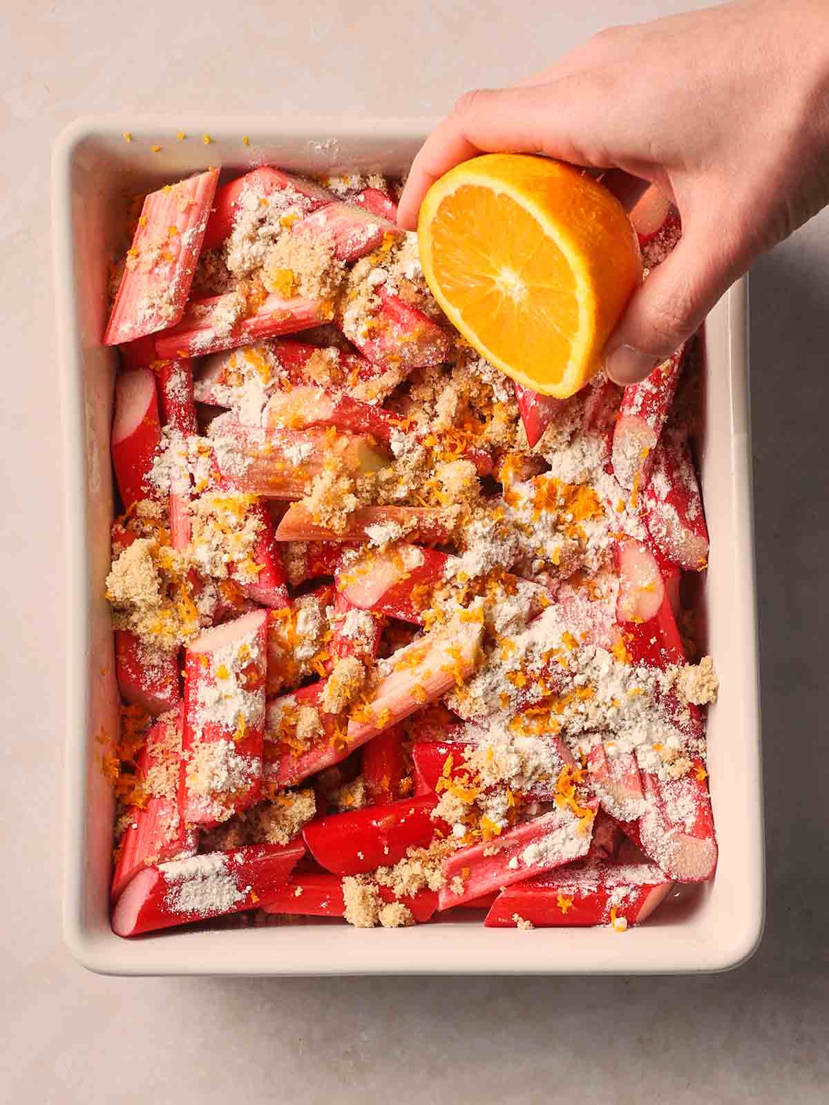 A hand squeezing over half an orange into rhubarb crumble filling before it's baked.