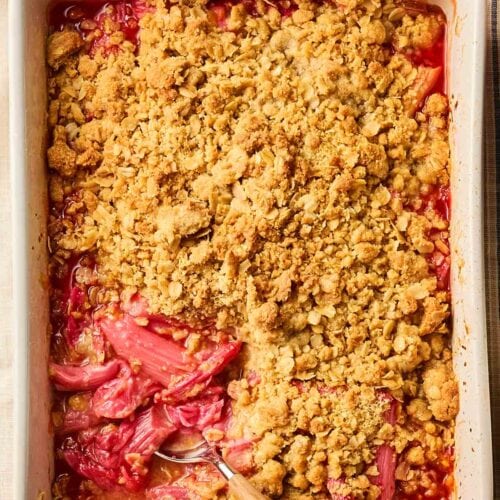 A traditional Rhubarb Crumble on a table with a stripy tablecloth, with a spoon ready to serve a portion.