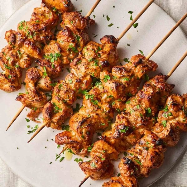 A close look at cookies and charred marinaded chicken kebabs, laid in a line on a white plate, with skewers through them.