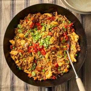 A black wok filled with Egg Fried Rice that's ready to eat, with a serving spoon, laid on a table with a blue and white stripy tablecloth.