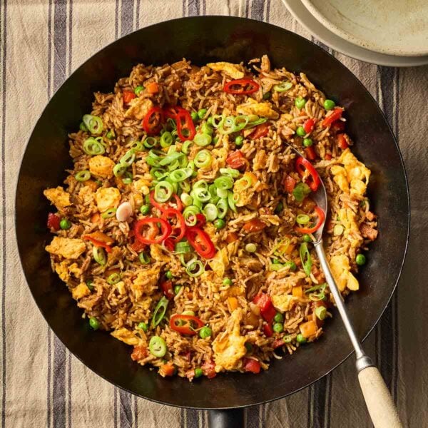 A black wok filled with Egg Fried Rice that's ready to eat, with a serving spoon, laid on a table with a blue and white stripy tablecloth.