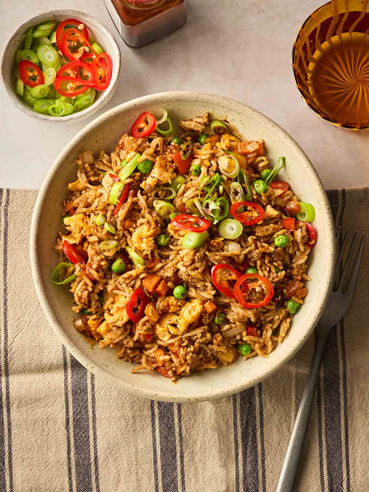 A bird's eye view of a table with a bowl of Egg Fried Rice with a fork to the side, and other dishes around it.
