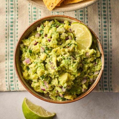 A bowl of guacamole with lime around the edges.