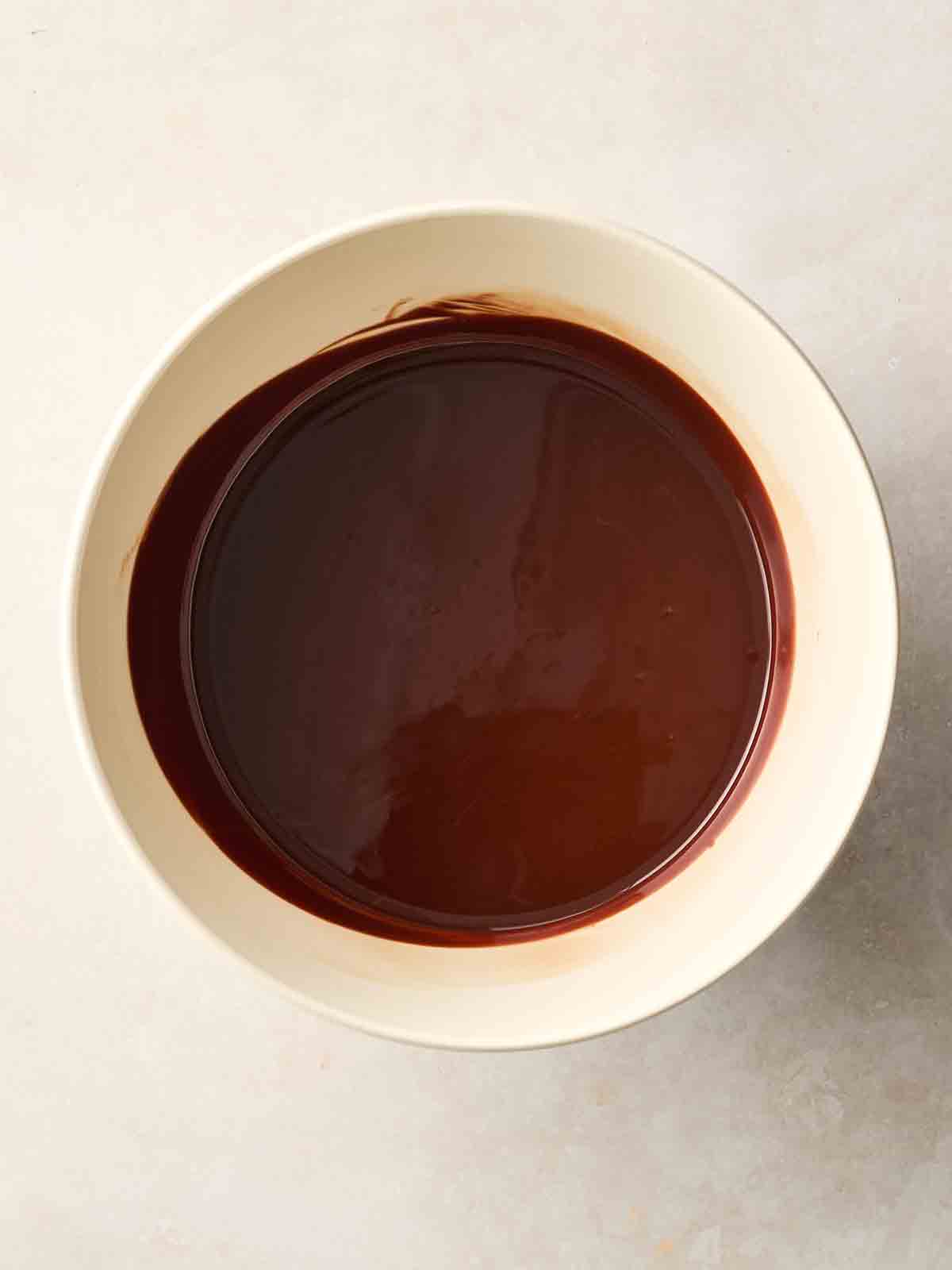 A white bowl with melted chocolate in, on a white surface.