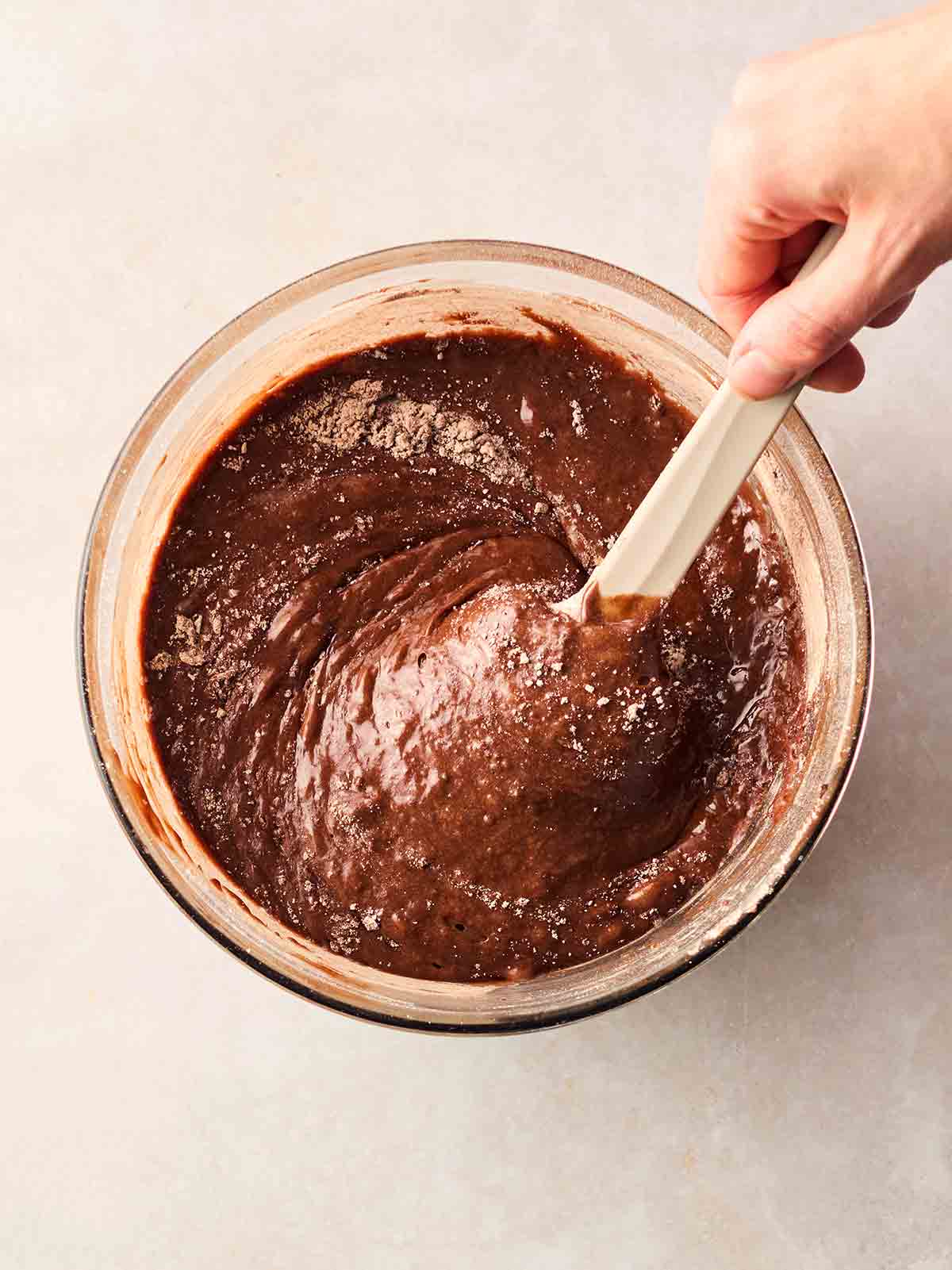 A hand stirring a mixture of brownie batter with oreo cookies inside.