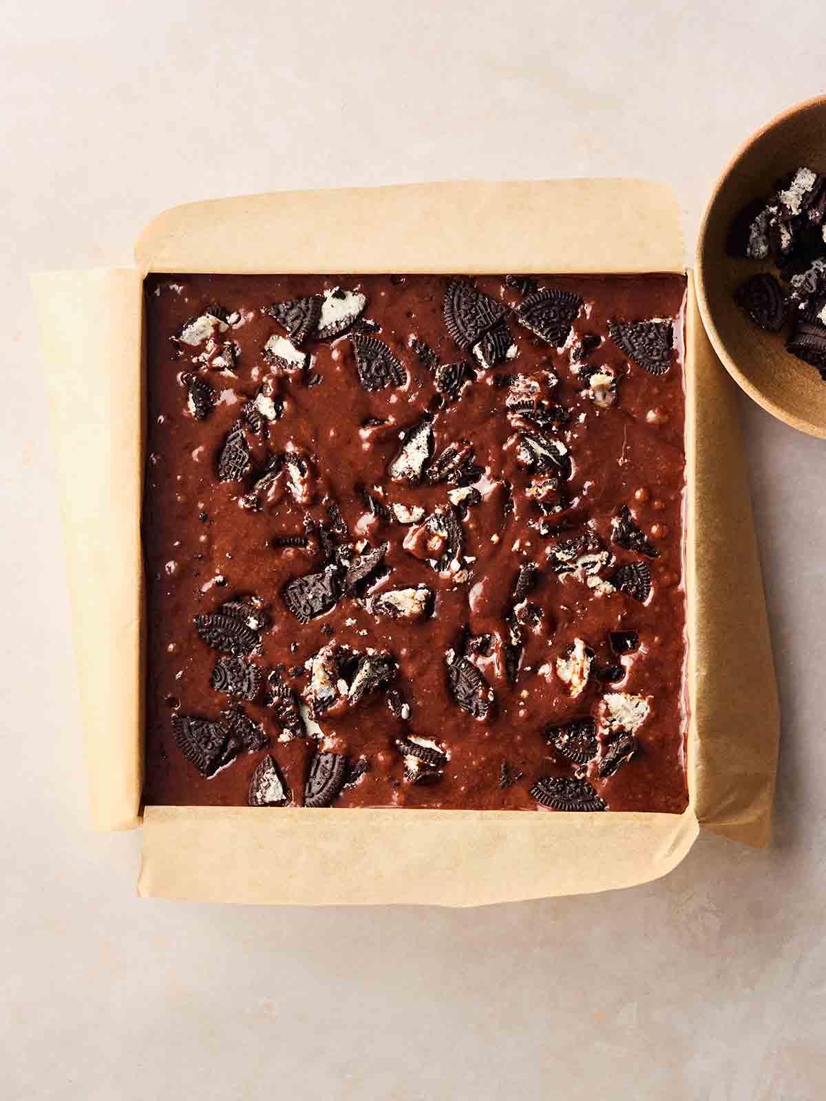 An unbaked square tin of Oreo brownies on a white surface.