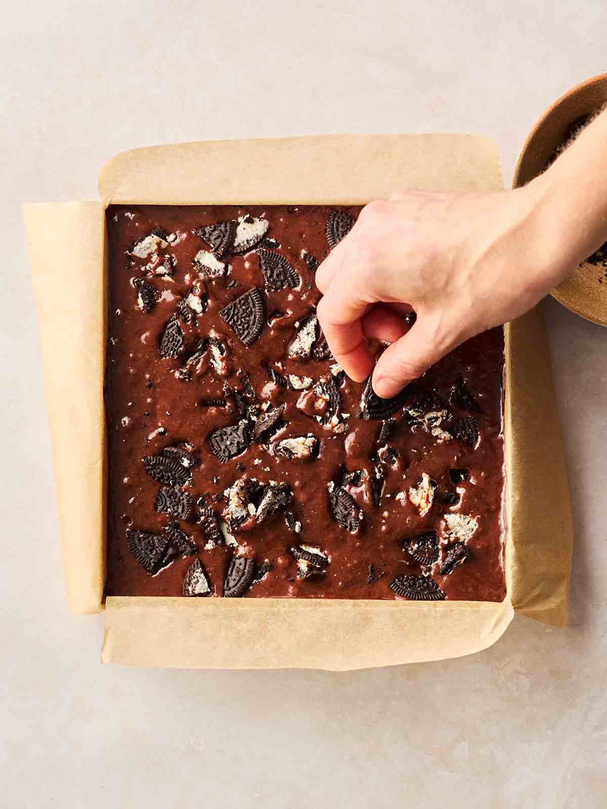 A hand putting Oreo Cookies on top of brownies mixture, ready for the oven.