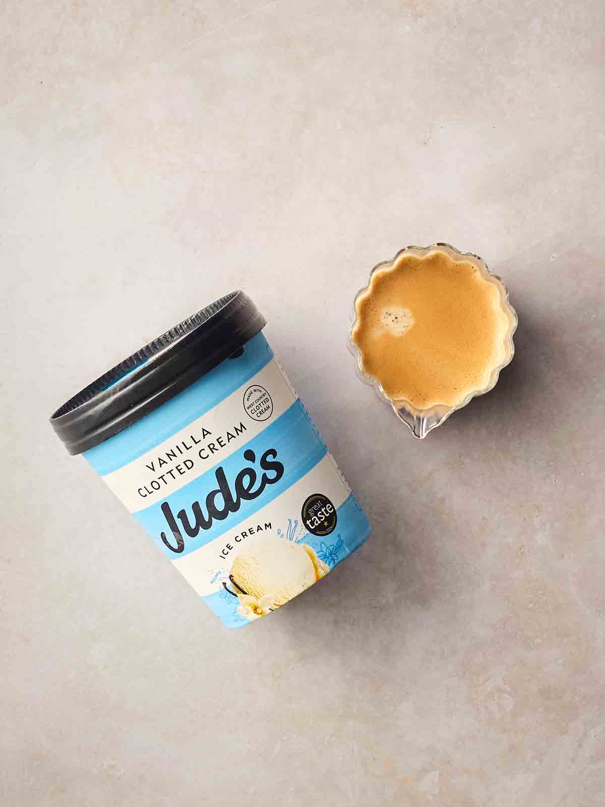 A tub of vanilla ice cream and a pot of espresso coffee on a white surface.