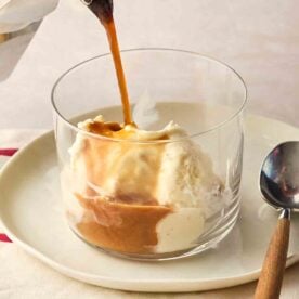 A glass of vanilla gelato with coffee being poured over to make a classic Italian dessert called Affogato. It's ready to eat with a spoon to the side.