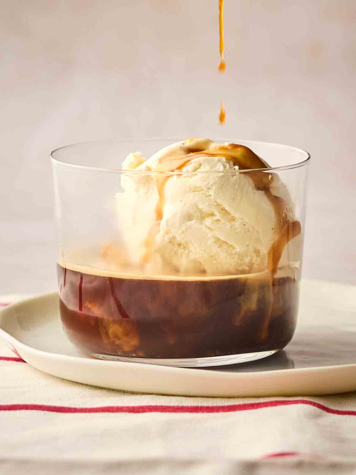 A drip of coffee going down onto vanilla ice cream and coffee in a dessert glass, on a plate, ready to eat at Affogato.