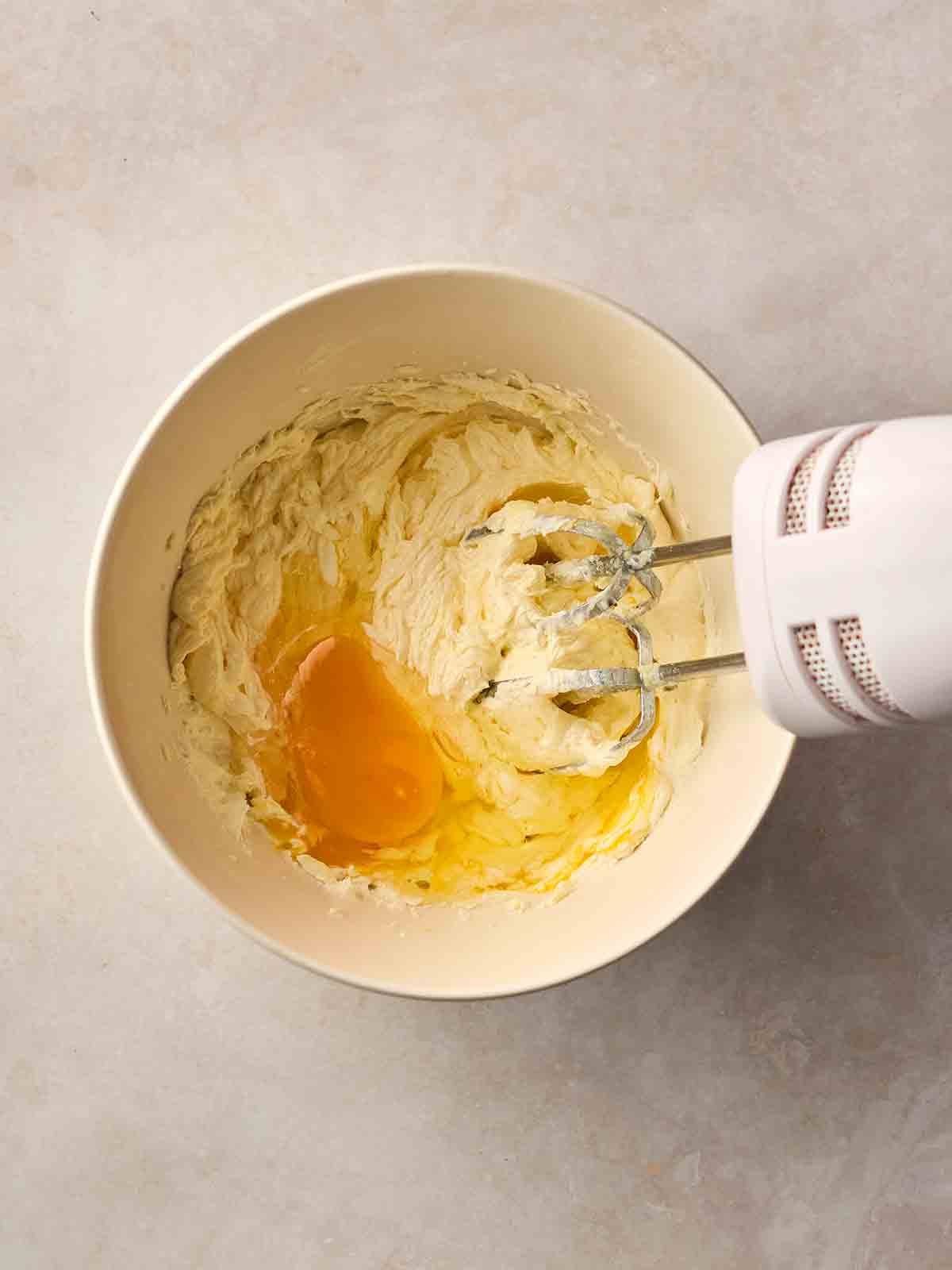 An electric whisk inside a cake mixture in a white bow,, with eggs ready to be mixed in.