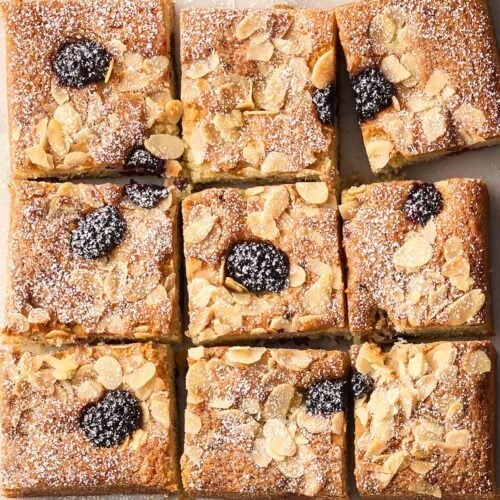 A blackberry cake with flaked almonds on top cut into squares.