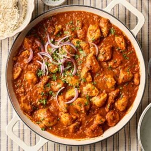 A large pan of homemade chicken curry with rice to the side, on top of a stripy tablecloth.