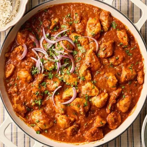 A pan of homemade curry with chicken on a stripy cloth, with side dishes, ready to serve.