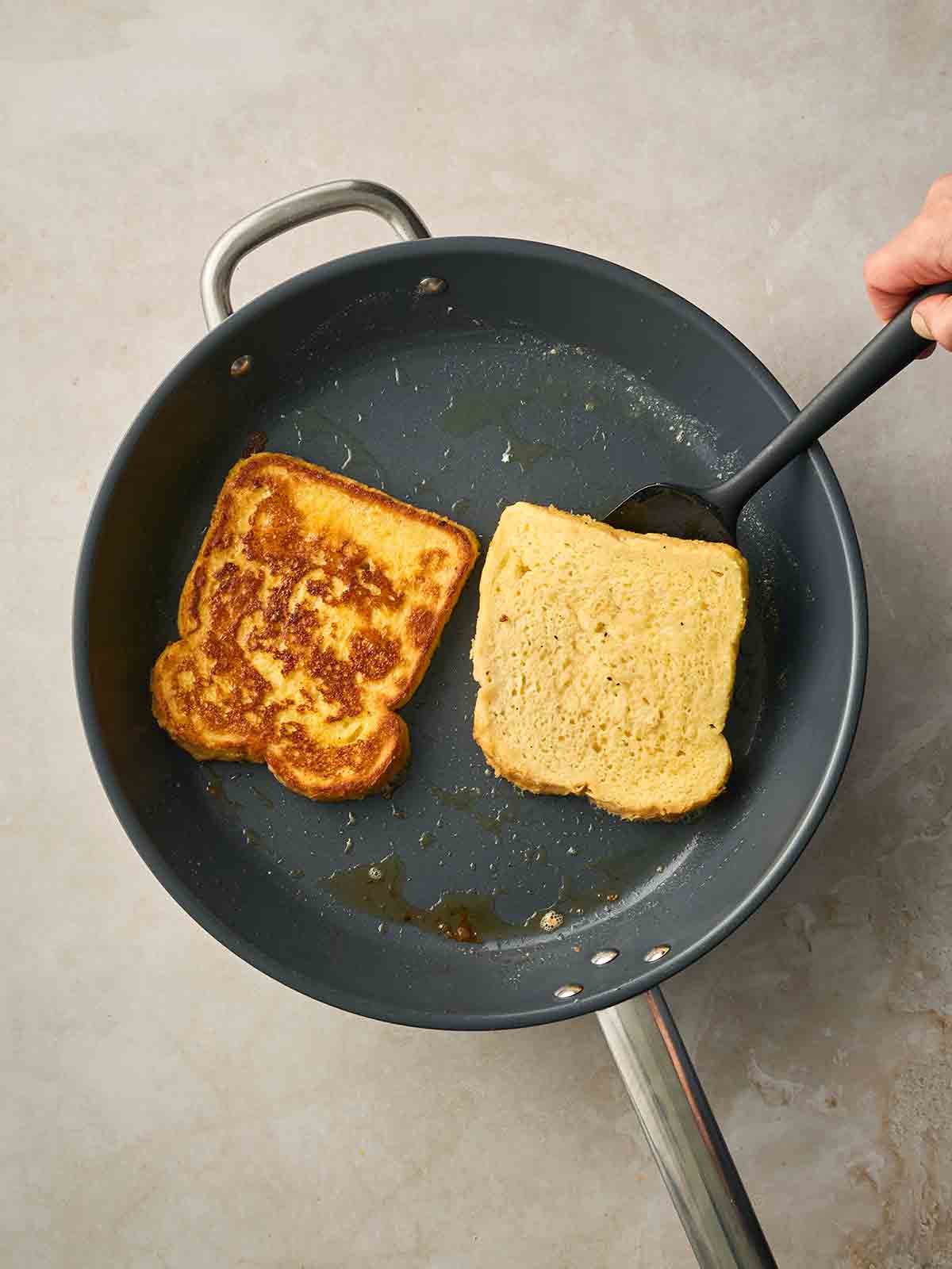 Two slices of white bread frying in a pan to make Eggy Bread.