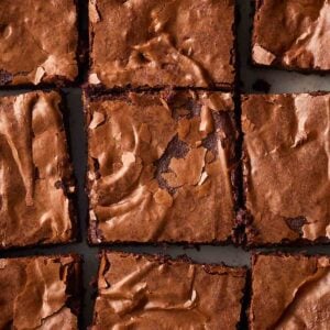 A close up of chocolate brownies with cracked tops, in squares.