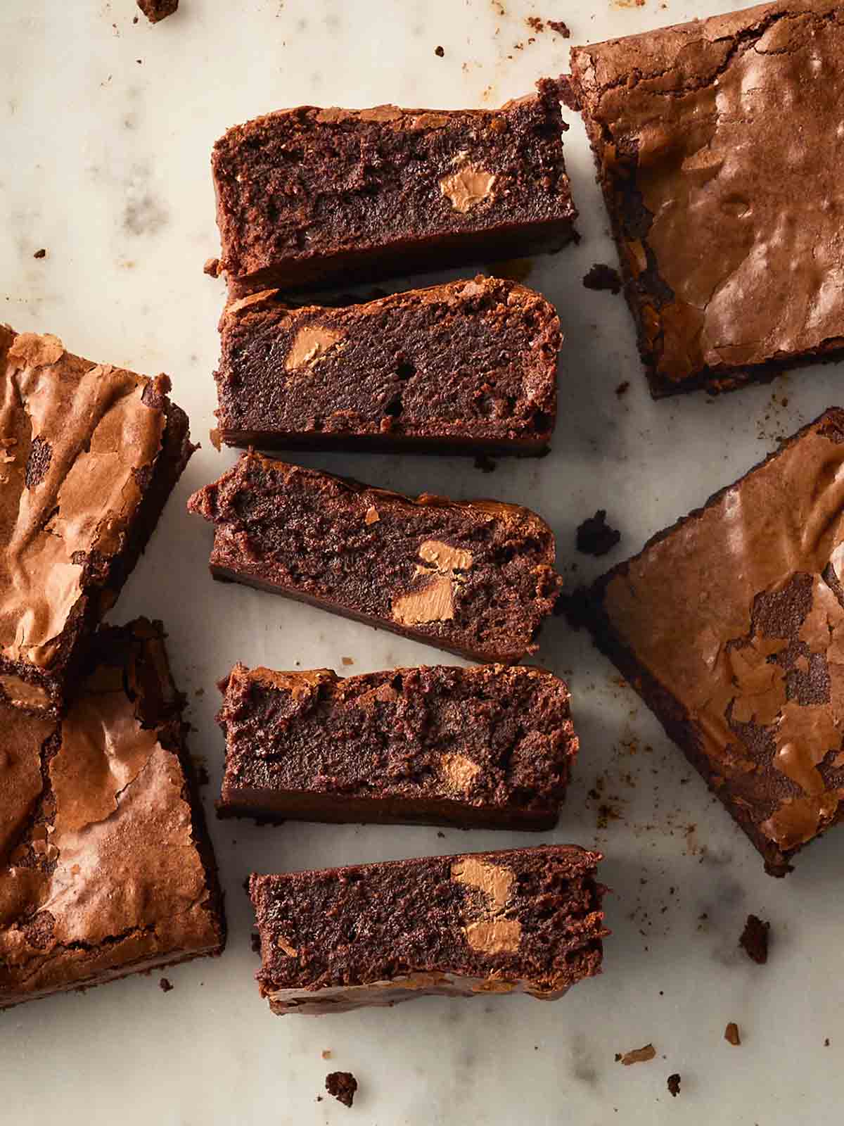 A row of fudgy brownies on their side on a white surface, revealing the gooey inside, with other pieces from the top.