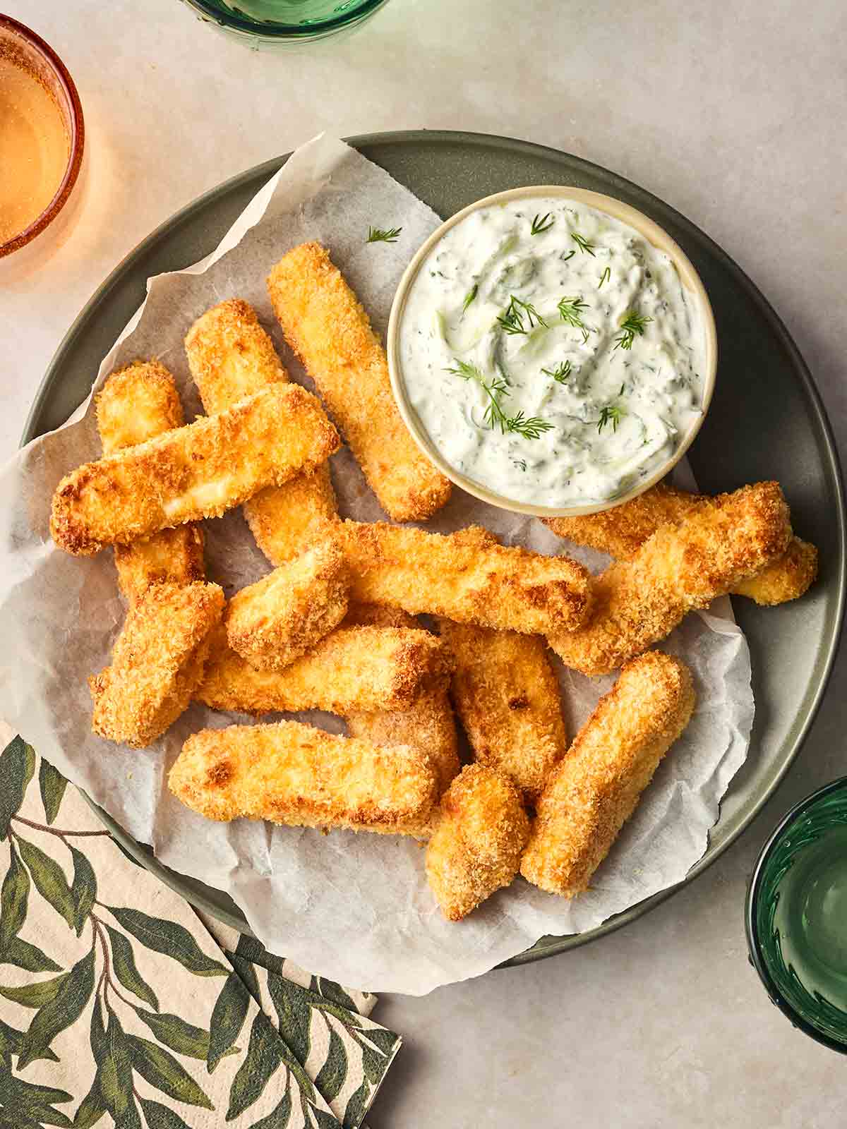 A plate of crispy and golden halloumi fries, with a bowl of dipping tzatziki, on a table with drinks.