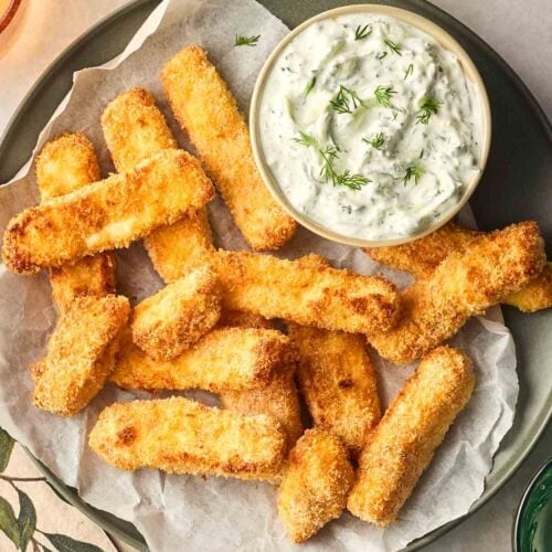 A plate filled with baked Halloumi Fries with a bowl of tzatziki to the side, on a table ready to eat.
