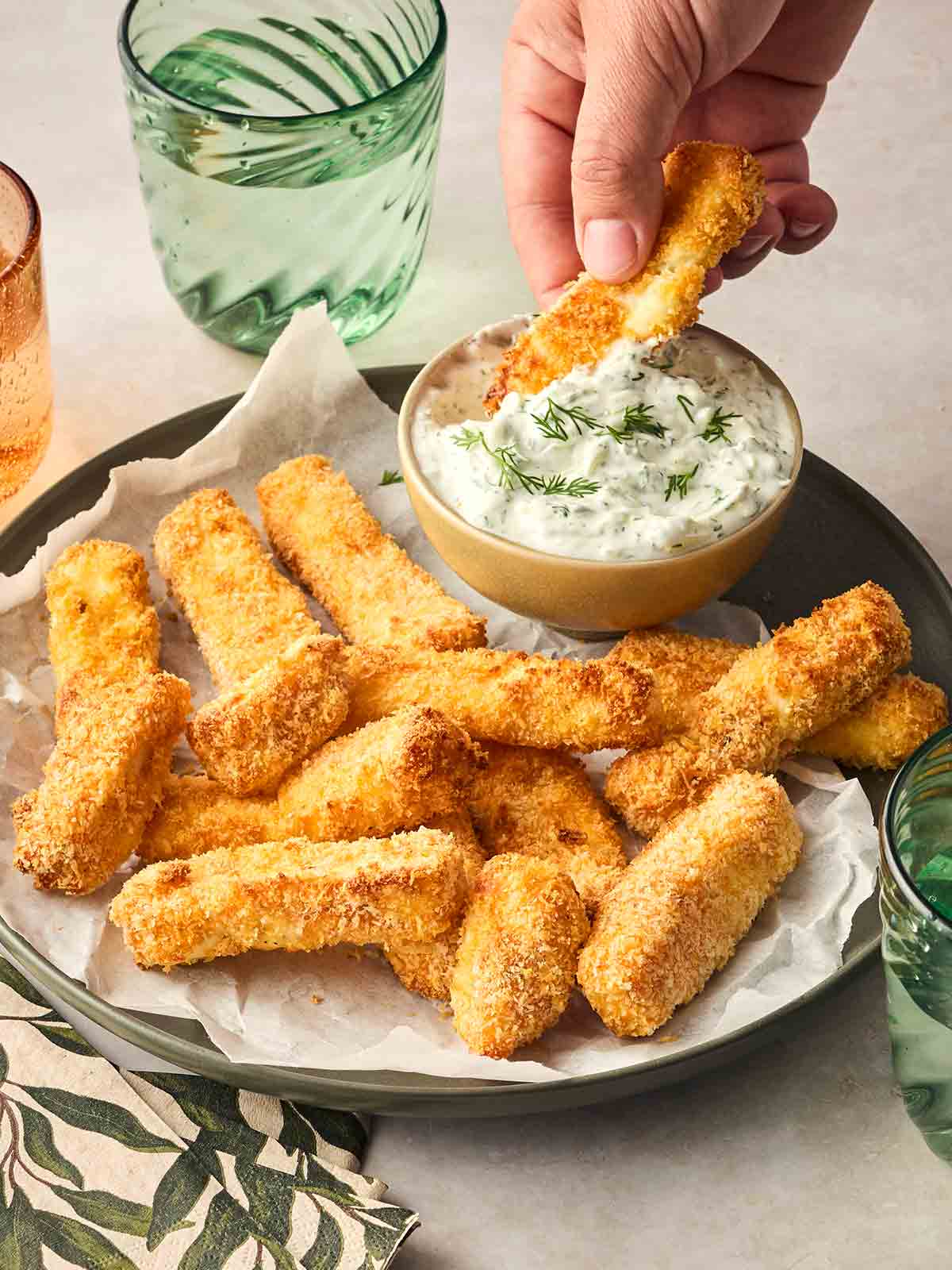 A hand dipping a coated halloumi fry in a bowl of tzatziki.