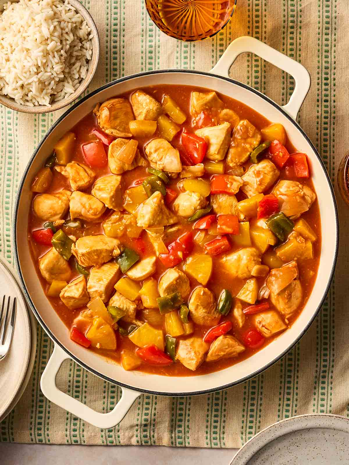 A large white pot of Sweet and Sour Chicken on a table with a bowl of rice to the side, ready to serve.