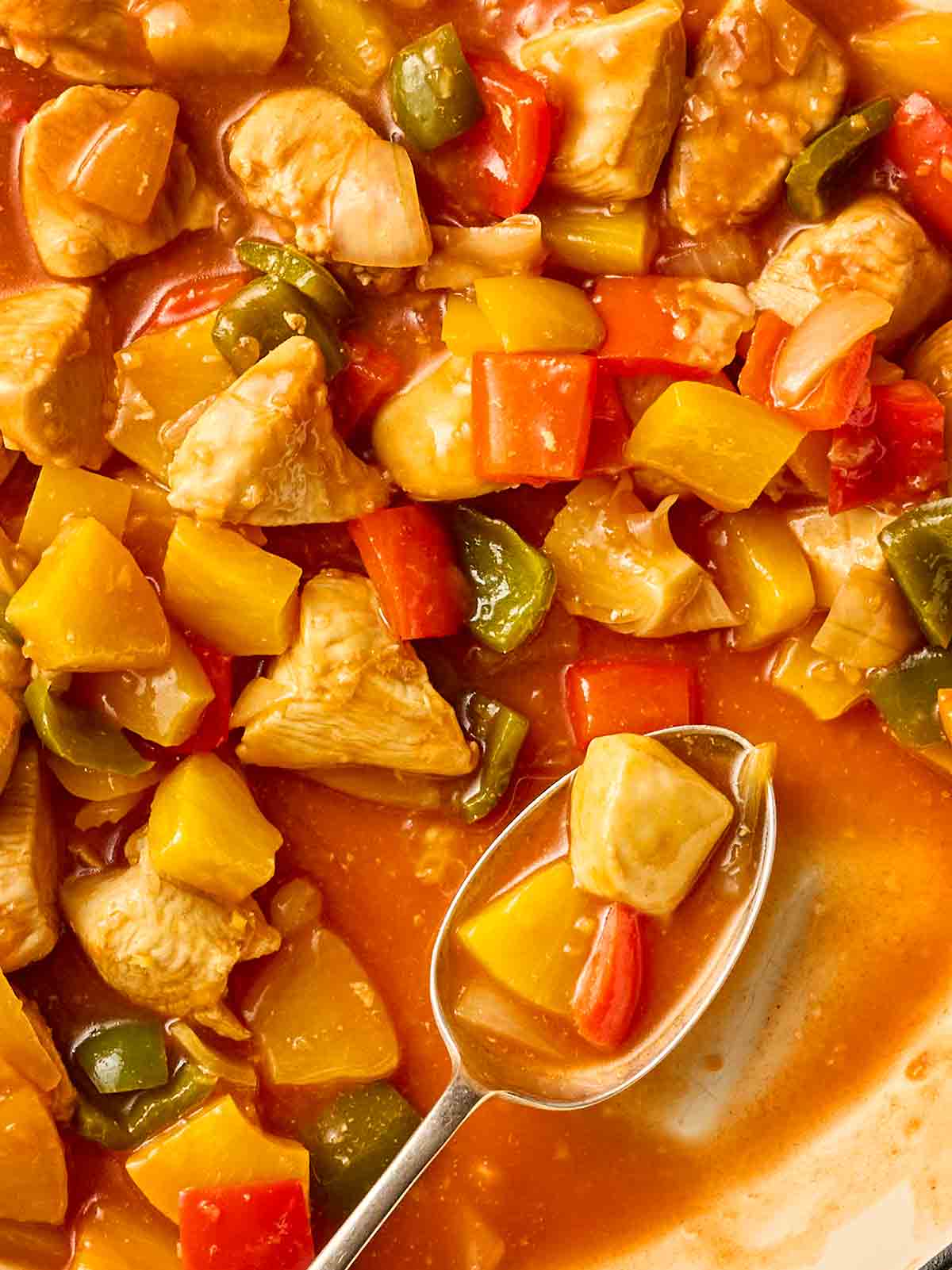 A spoon in a pot of homemade Sweet and Sour Chicken, ready to dish out.