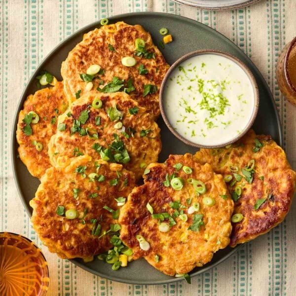 A plate of Sweetcorn Fritters with a yoghurt dip, on a tablecloth with green stripes, ready to serve.