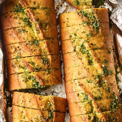 A baguette cut in two, made into garlic bread, inside a foil package.