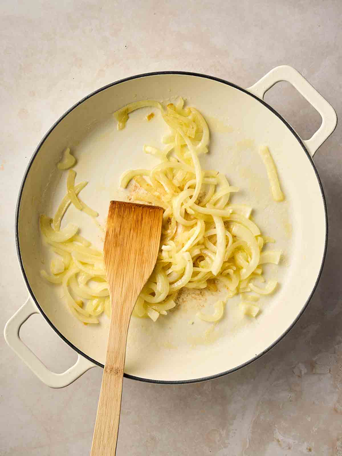 A pan of sliced onions, frying with a wooden spatula in.