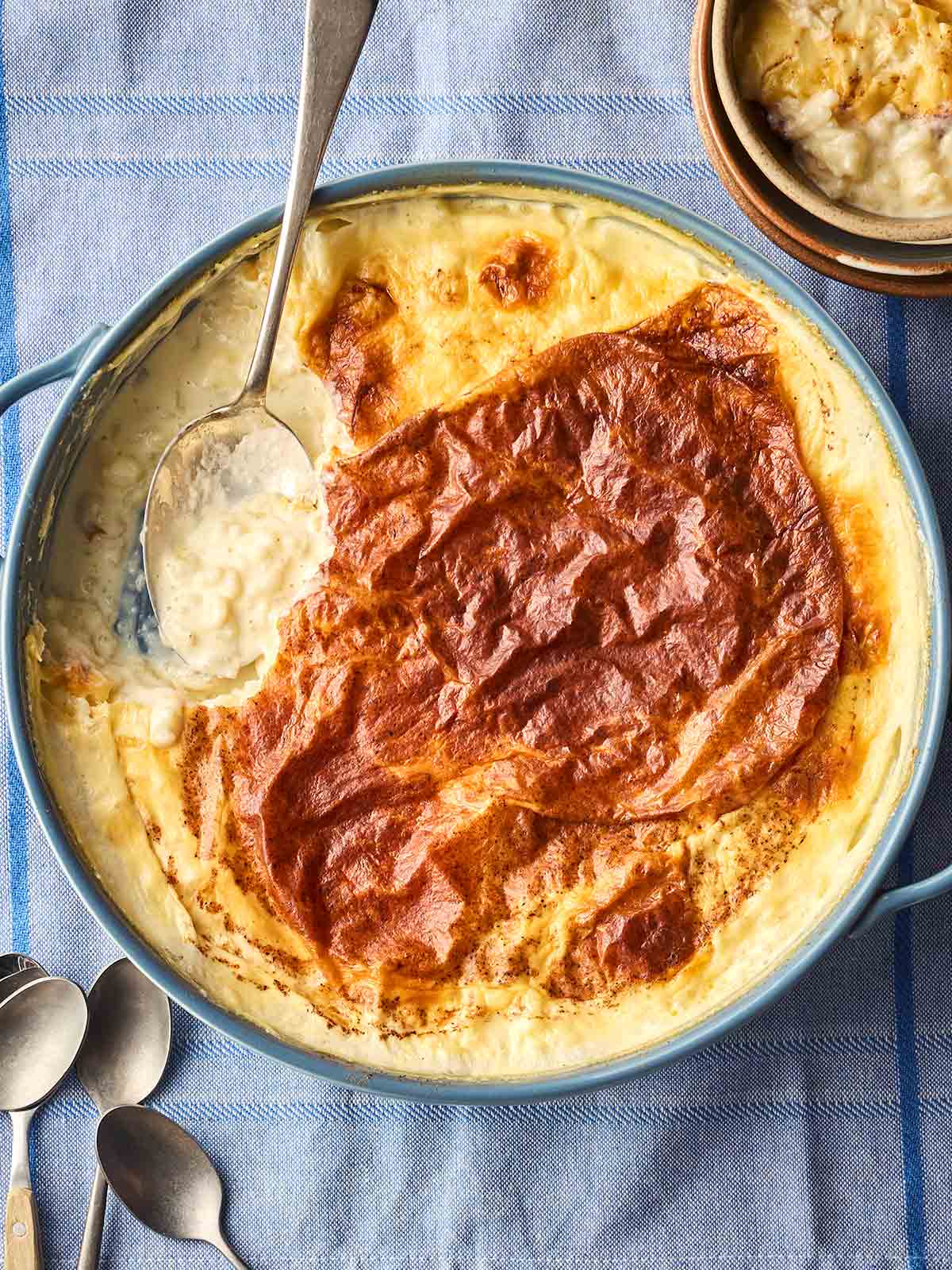 A classic oven-baked rice pudding with a skin on top, in pan, on a table, ready to be served with a spoon.