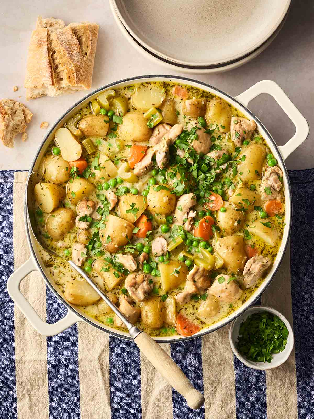 A large pan filled with hearty Chicken Stew and chunky bread to the side, on a table ready to serve.