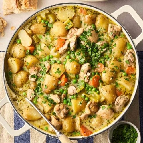 A large pot of stew with chicken, potatoes and vegetables in a rich broth, with parsley and bread on the side, ready to serve into bowls.