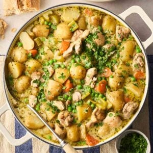 A large pan filled with cooked Chicken Stew, packed with vegetables, herbs, chicken chunks and parsley on top in a rich, creamy broth.