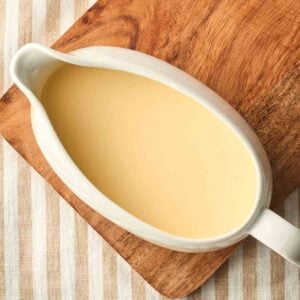 A jug of homemade custard ready to pour, on a board on a table.