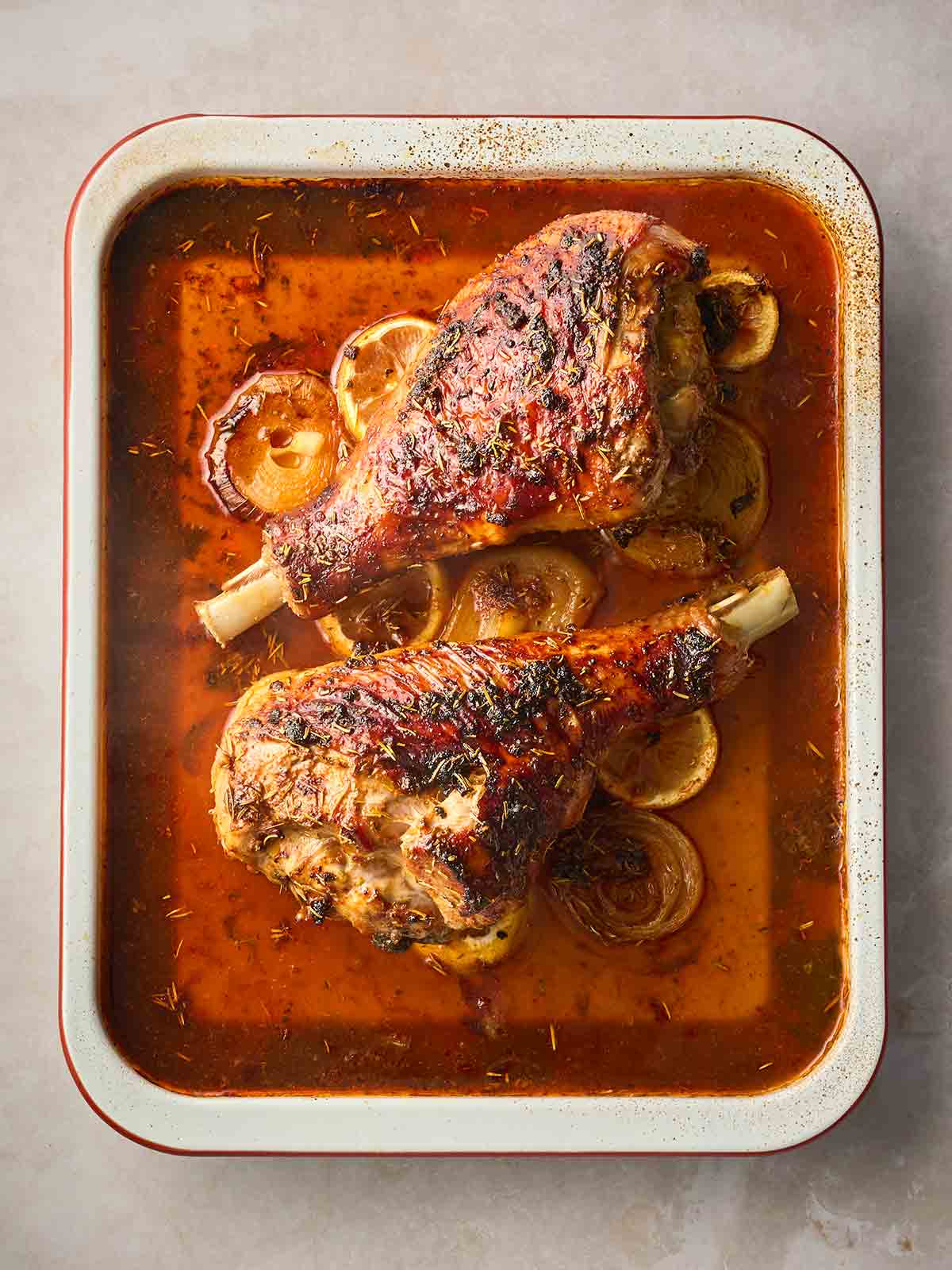 A baking tray with roast turkey legs on top and a reddish brown sauce underneath.