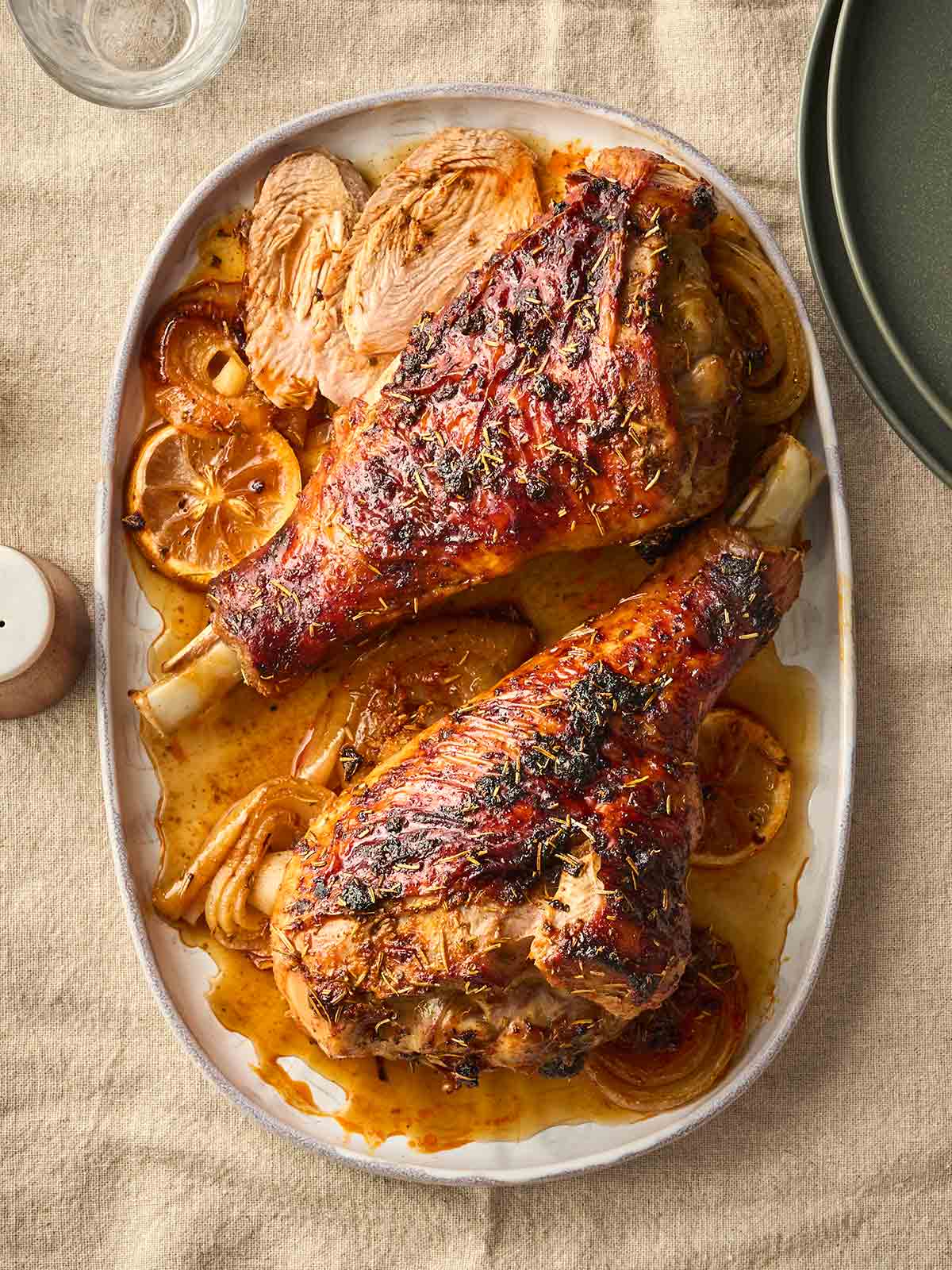 Two roasted turkey legs on a tray, surrounding by a sauce of lemon and onion, ready to serve.