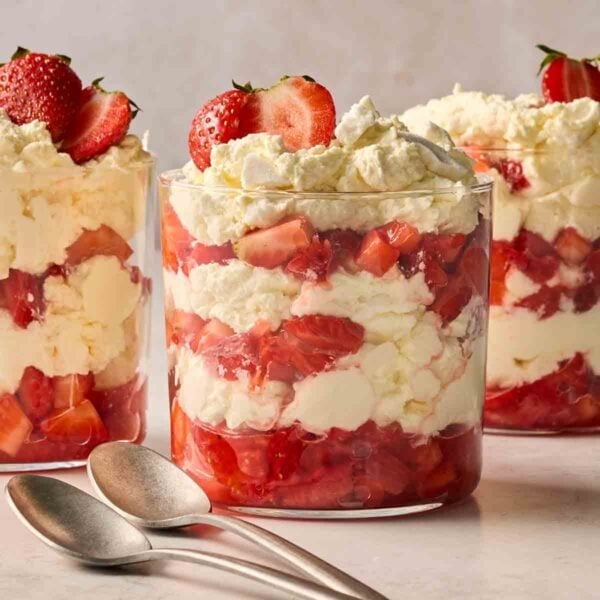 Three Eton Mess desserts on a white counter, with layers of cream, meringue and strawberries showing.