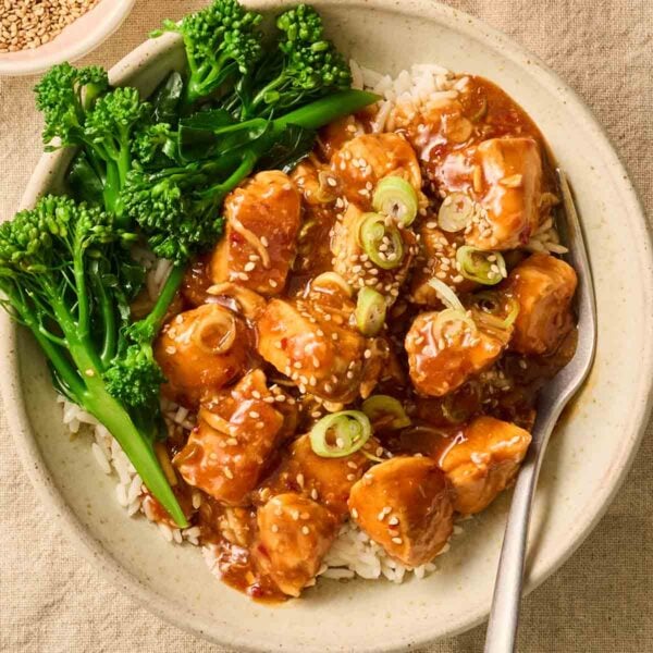 A close up of a plate of honey garlic chicken in a sauce with broccoli and rice, with a fork.