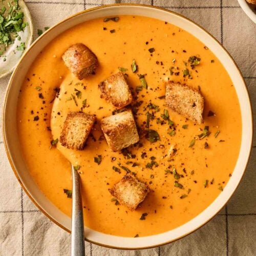 An orange vegetable soup on a table, ready to eat.